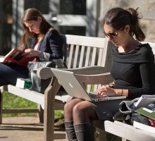 Syracuse student sitting on a bench with laptop
