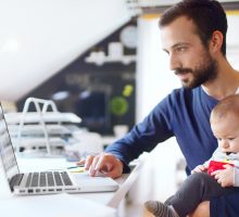 Online Degree - Father working on laptop with infant sitting on lap